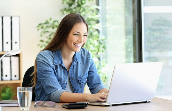 beautiful woman typing while smiling at laptop - devicenow. True subscription worldwide
